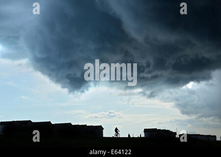 Les nuages de tempête brew plus de cabanes de plage et bateaux sur le front de mer à Goring, West Sussex, que les cyclistes et les gens marchent par Banque D'Images