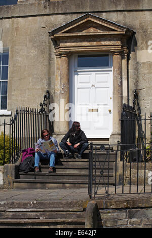 Couple assis sur des marches à l'extérieur du 30 Royal Crescent regardant la brochure de la littérature d'information à Bath, Somerset Royaume-Uni en avril Banque D'Images