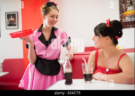 Une serveuse vêtue de style des années 1950 American retro fashion vêtements desservant une clientèle féminine dans un diner UK Banque D'Images