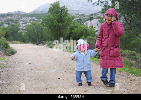 Jeune enfant tenant la main d'un bambin sur marcher sur un chemin forestier Banque D'Images