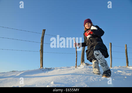 Fille qui marche par une clôture holding boules de neige sur un jour d'hiver enneigé Banque D'Images