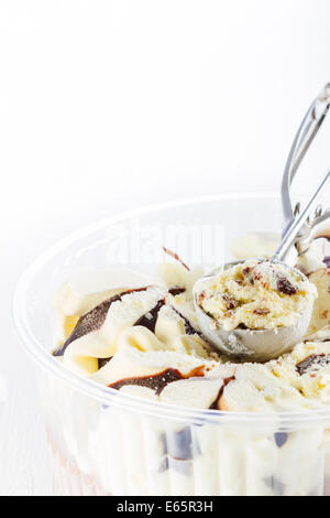 Avec la vanille glace chocolat écope creusées dans d'un conteneur sur fond de bois blanc Banque D'Images