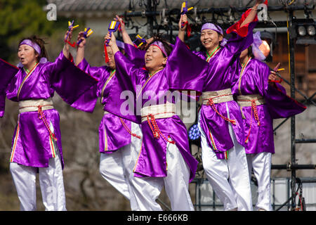 Six danseuses japonaises Yosakoi vêtues de robes de yukata pourpres et de pantalons blancs, dansant sur scène et tenant naruko, des trappeurs en bois. Kumamoto. Banque D'Images
