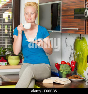 Très belle jeune femme blonde caucasienne de boire du café dans la cuisine de maison confortable Banque D'Images