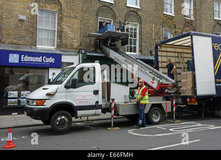 Les hommes de l'absorption à l'aide d'ascenseur pour élever possessions à la fenêtre du premier étage, Londres Banque D'Images