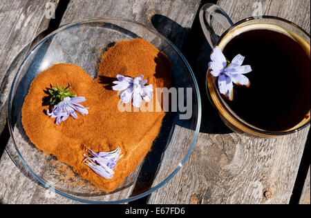 Poudre de chicorée comme forme de cœur sur la plaque avec des fleurs de chicorée chicorée et boire dans la tasse sur un bureau en bois Banque D'Images