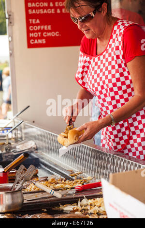 Poireau & DISTRICT SHOW, poireau, Staffordshire, Angleterre Une femme portant un tablier rouge à carreaux servant un hot-dog à partir d'un restaurant Banque D'Images