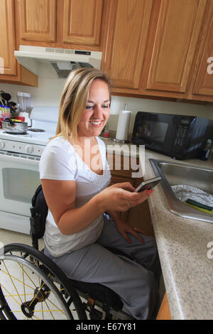 Femme avec de la moelle épinière dans sa cuisine accessible à l'aide d'un téléphone mobile Banque D'Images