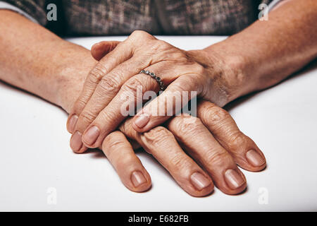 Macro d'une vieille dame assise avec elle les mains jointes sur une table. Les mains de vieille femme avec un anneau reposant sur la surface grise. Banque D'Images