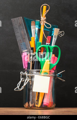 Accessoires de l'école dans un pot sur le bureau avec tableau noir dans l'arrière-plan Banque D'Images