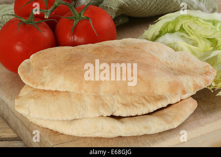 Pile de trois pains pitta frais sur une planche en bois avec laitue et tomates Banque D'Images