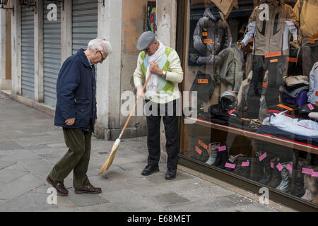 Deux hommes plus âgés parlent pendant un matin dans l'avant du magasin sur une rue piétonne principale de Venise. Banque D'Images