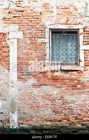 Vieux mur de briques et de fenêtre en fer forgé sur l'un des canaux de Venise. Banque D'Images