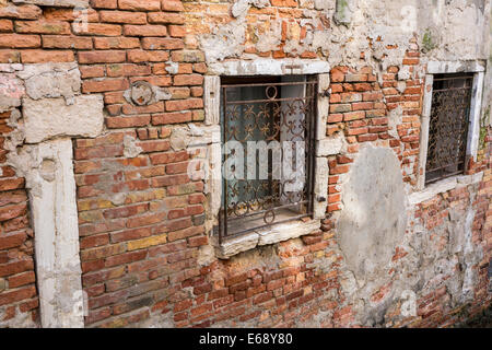 Vieux mur de briques et de fenêtres en fer forgé sur l'un des canaux de Venise. Banque D'Images