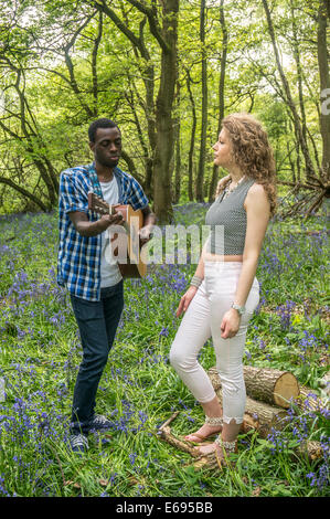 Couple interracial. Une jolie adolescente chantant avec son beau mec qui joue de la guitare. And Banstead, Woods and Banstead, Surrey, Angleterre, Royaume-Uni. Banque D'Images