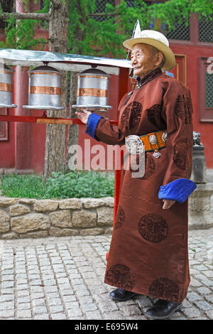 Un homme âgé portant un deel traditionnel tout en faisant tourner les roues de prière bouddhiste dans le monastère de Gandan, Ulaanbaatar, Mongolie Banque D'Images