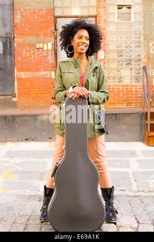 Mixed Race woman with guitar case on city street Banque D'Images