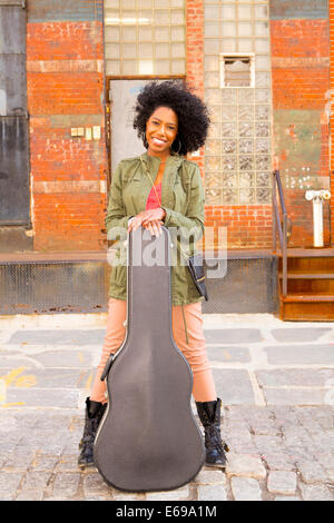 Mixed Race woman with guitar case on city street Banque D'Images