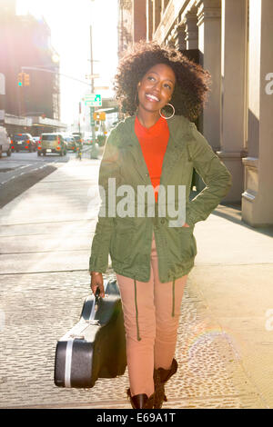 Mixed Race woman carrying guitar case sur le trottoir de la ville Banque D'Images