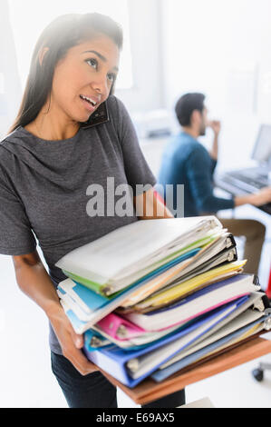 Hispanic businesswoman carrying stack of folders in office Banque D'Images