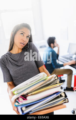 Hispanic businesswoman carrying stack of folders in office Banque D'Images