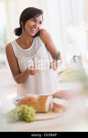 Hispanic Woman talking on cell phone et la cuisson dans la cuisine Banque D'Images