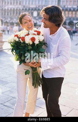 Man giving girlfriend flowers on city street Banque D'Images