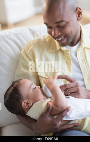 Nourrir bébé père Smiling on sofa Banque D'Images