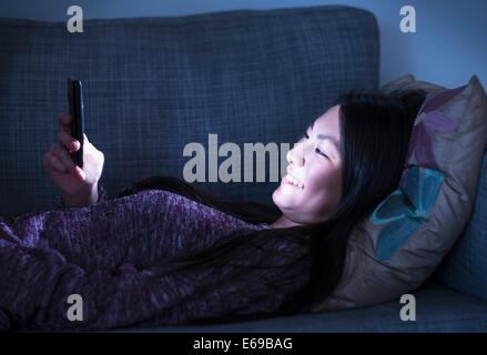 Mixed Race teenage girl using cell phone on sofa Banque D'Images