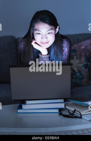 Mixed Race teenage girl using laptop on sofa Banque D'Images