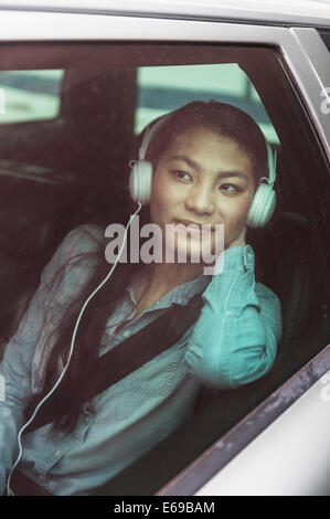 Mixed Race woman listening to headphones in backseat of car Banque D'Images