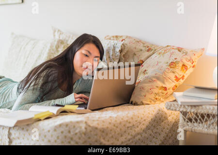 Mixed Race girl doing homework on bed Banque D'Images