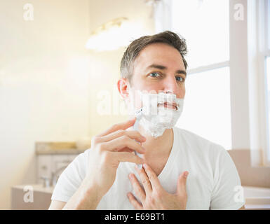 Caucasian man shaving in bathroom Banque D'Images