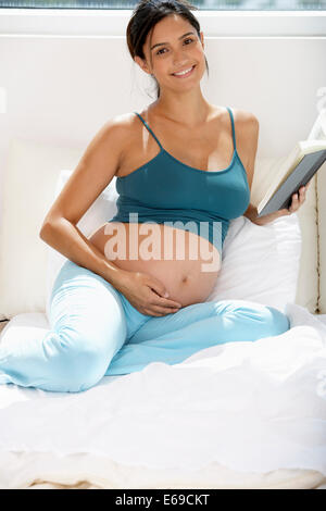 Pregnant Hispanic woman reading in bed Banque D'Images