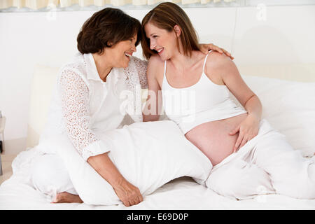 Mother hugging pregnant daughter on bed Banque D'Images