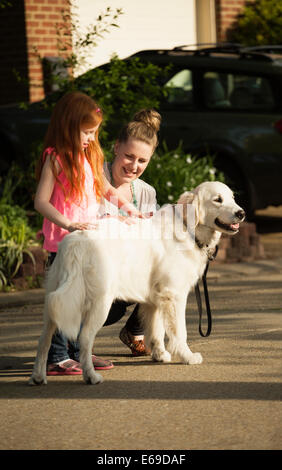 Caucasian mother and daughter petting dog on Rue de banlieue Banque D'Images