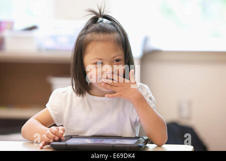 Mixed Race Down syndrome student using tablet computer in classroom Banque D'Images