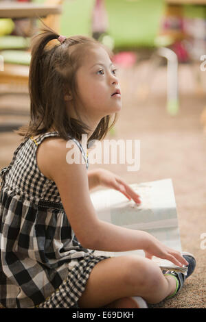 Mixed Race Down syndrome student sitting on floor Banque D'Images