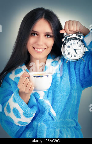 Jeune femme en peignoir détenant un réveil et une tasse de café Banque D'Images