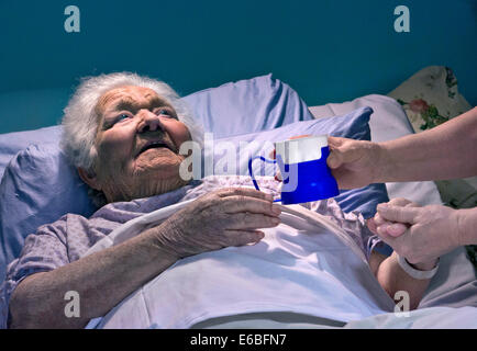 Lady âgée de vieillesse souriante et souriante dans le lit d'hôpital réconfortant la main de l'infirmière de soignant avec hydratation hydratant tasse d'eau fraîche Banque D'Images