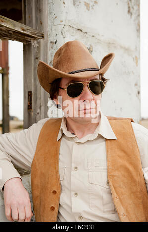 Portrait of a modern day cowboy, appuyé contre le cadre de la fenêtre d'un bâtiment abandonné. Banque D'Images