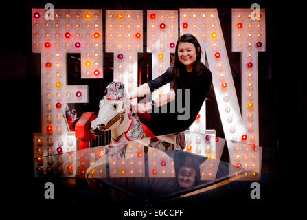 Olivia Yip assise sur son parc d'cheval devant un signe de plaisir du jeu à ses illuminations Hastings shop. Banque D'Images