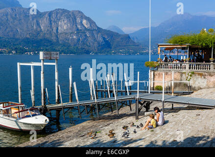 Mère et fils se nourrir les canards et les pigeons sur le bord du lac à Bellagio, Lac de Côme, Lombardie, Italie Banque D'Images