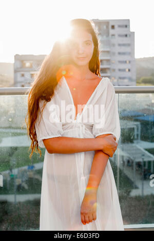 Jeune femme confiante dans son 20s avec de longs cheveux bruns en robe blanche. Par le soleil en contre-jour. Autorisation modèle disponible Banque D'Images