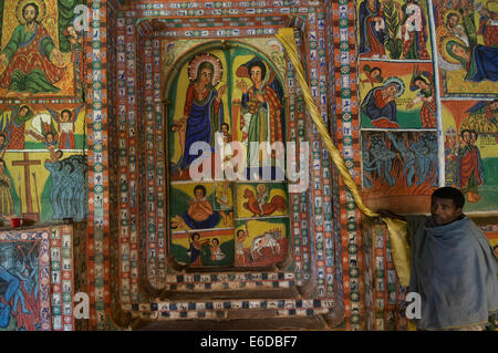 Prêtre montrant outre de peintures murales religieuses peint de couleurs vives sur le saint des saints dans l'intérieur de l'Ura Kidane Mehret église sur la péninsule de Zege, Lac Tana, Bahir Dar, Ethiopie Banque D'Images