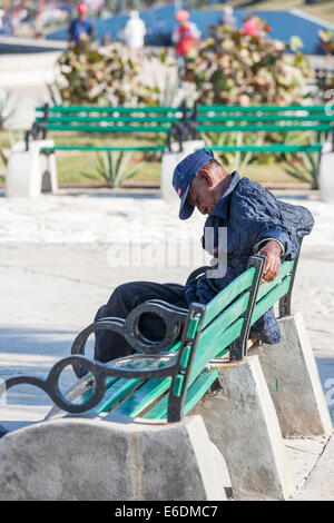 Ancien local homme cubain sommeille au soleil sur un banc vert sur le Malecon, La Havane, Cuba Banque D'Images