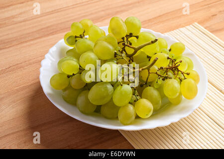 De délicieux raisins frais en plaque blanche sur fond de bois. Banque D'Images