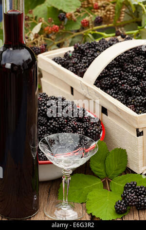 Les mûres mûres dans un bol et de fruits et une bouteille de liqueur de mûre avec un verre Banque D'Images