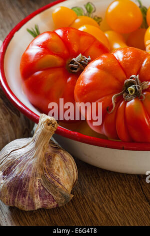 Les tomates fraîchement cueillies dans un bol de l'émail et la viande un bulbe d'ail Banque D'Images