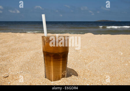 Café glacé avec une paille dans le sable sur la plage. Banque D'Images